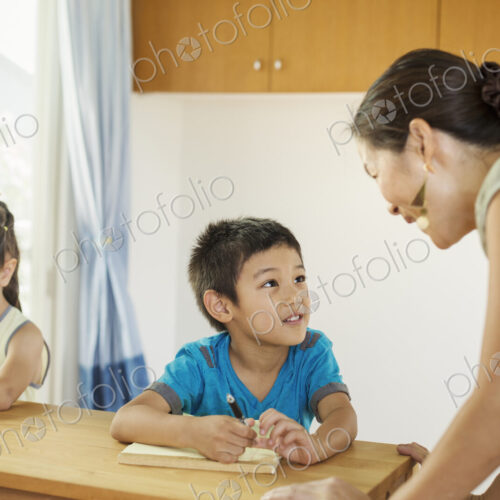 A teacher talking to two children sitting at a desk.