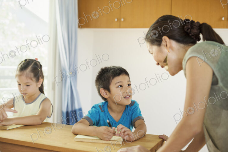 A teacher talking to two children sitting at a desk.