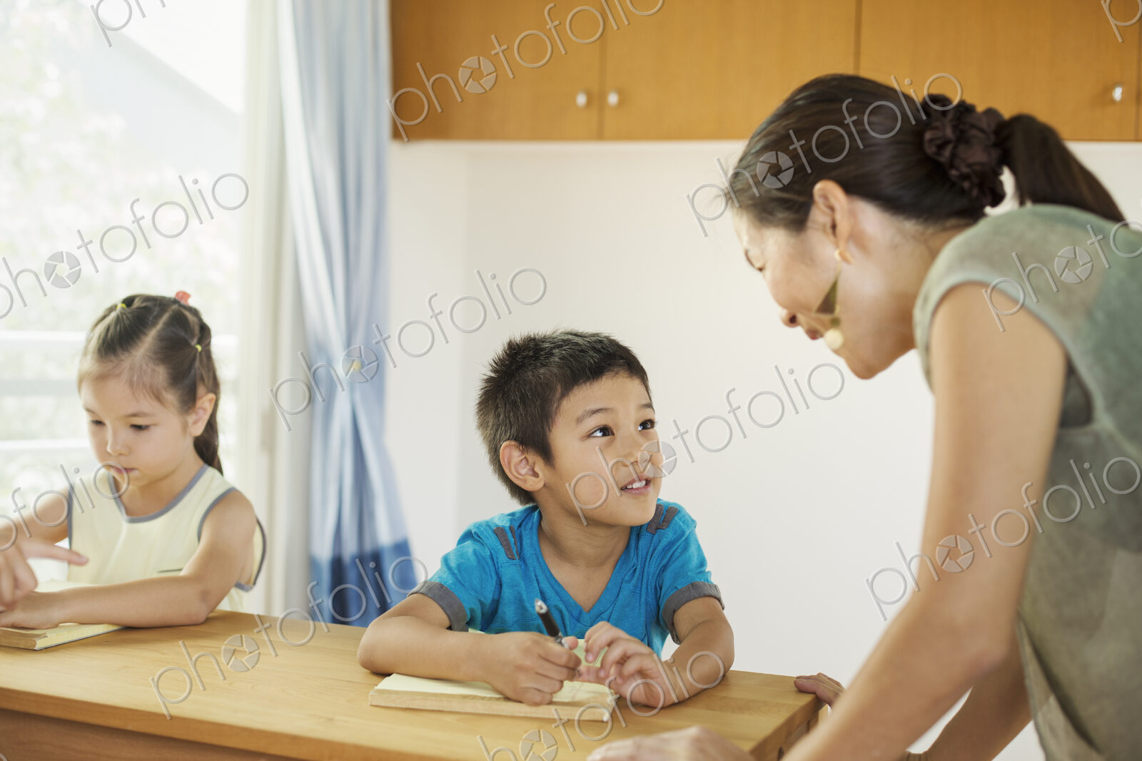 A teacher talking to two children sitting at a desk.