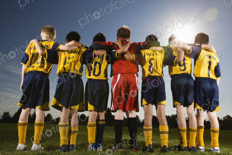 A team of soccer players standing in a row, arms around each other.