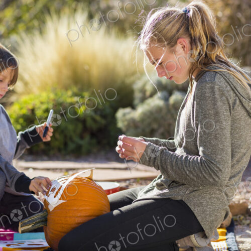 A teenage girl and a boy carving pumpkins at Halloween.