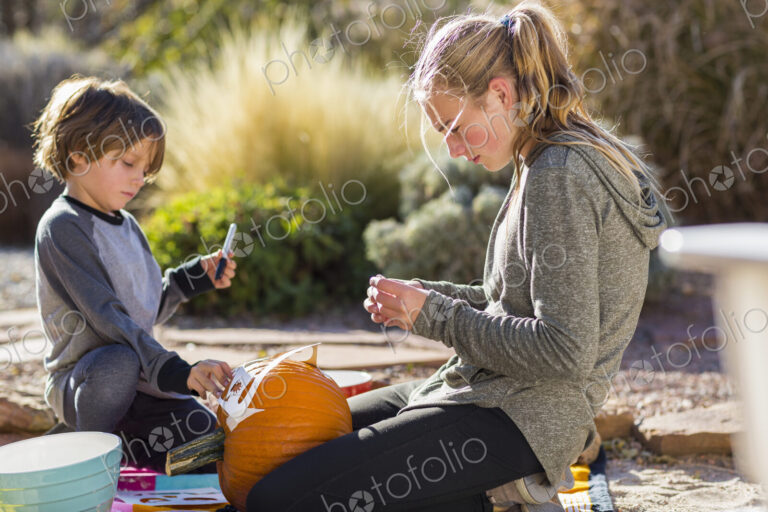 A teenage girl and a boy carving pumpkins at Halloween.