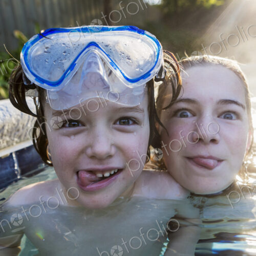 A teenage girl and brother in a warm pool, looking at the camera, sticking their… A teenage girl and brother in a warm pool, looking at the camera, sticking their…
