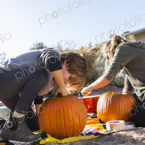 A teenage girl and her brother carving pumpkins at Halloween.