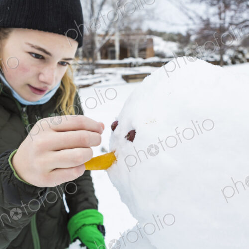 A teenage girl building a snowman adding nose and eyes A teenage girl building a snowman adding nose and eyes