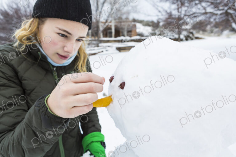 A teenage girl building a snowman adding nose and eyes