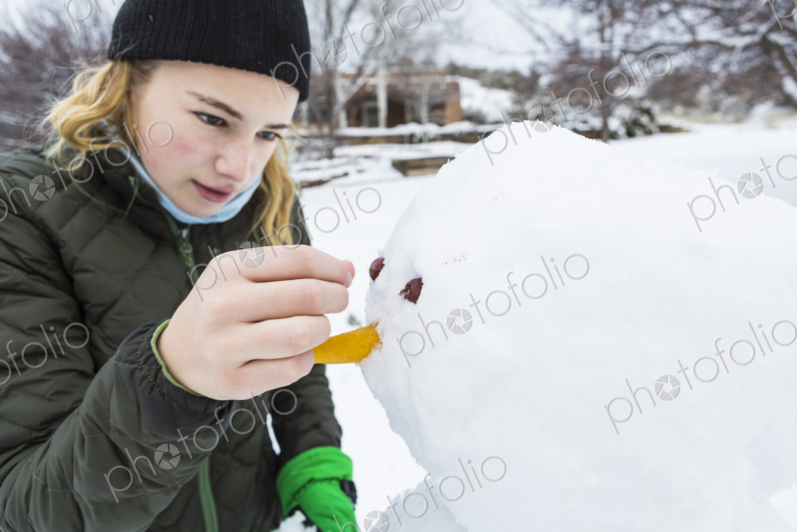 A teenage girl building a snowman adding nose and eyes
