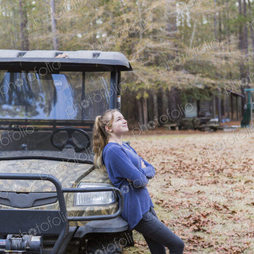 A teenage girl by an all terrain vehicle, a buggy, leaning with arms folded.