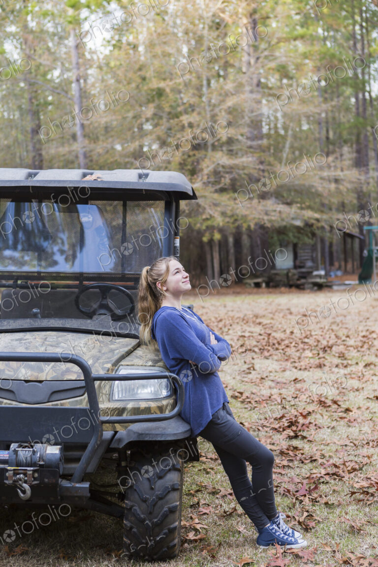 A teenage girl by an all terrain vehicle, a buggy, leaning with arms folded.