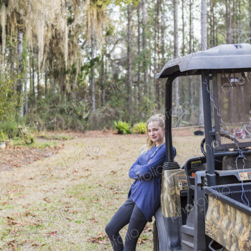A teenage girl by an all terrain vehicle, a buggy, leaning with arms folded.
