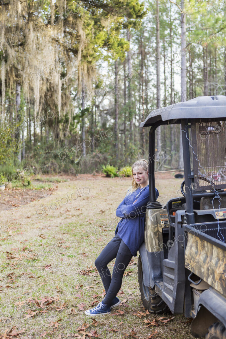 A teenage girl by an all terrain vehicle, a buggy, leaning with arms folded.