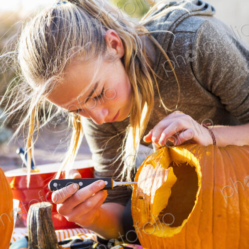 A teenage girl carving a large pumpkin at Halloween.