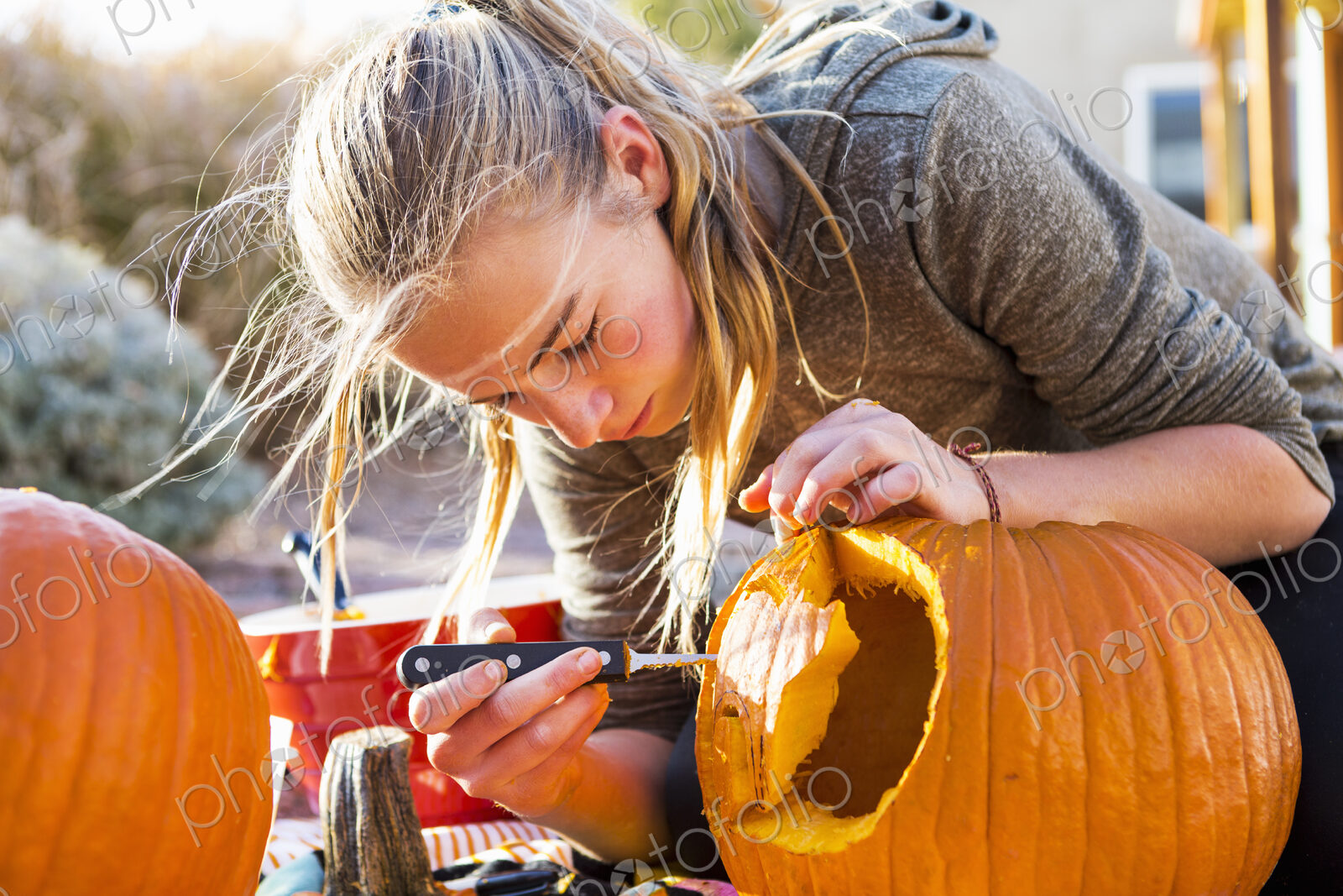 A teenage girl carving a large pumpkin at Halloween.