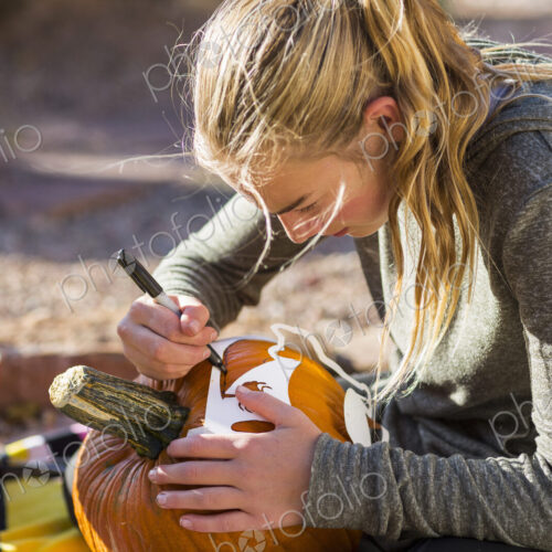 A teenage girl carving pumpkin outdoors at Halloween.