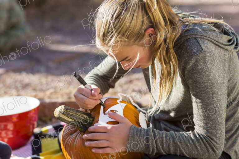 A teenage girl carving pumpkin outdoors at Halloween.