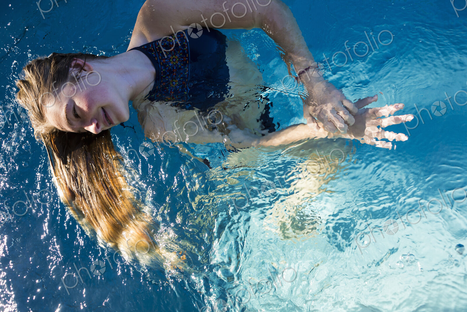 A teenage girl in a swimming pool, her long blond hair fanning out in the water.