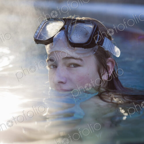A teenage girl in a swimming pool wearing goggles, steam rising A teenage girl in a swimming pool wearing goggles, steam rising