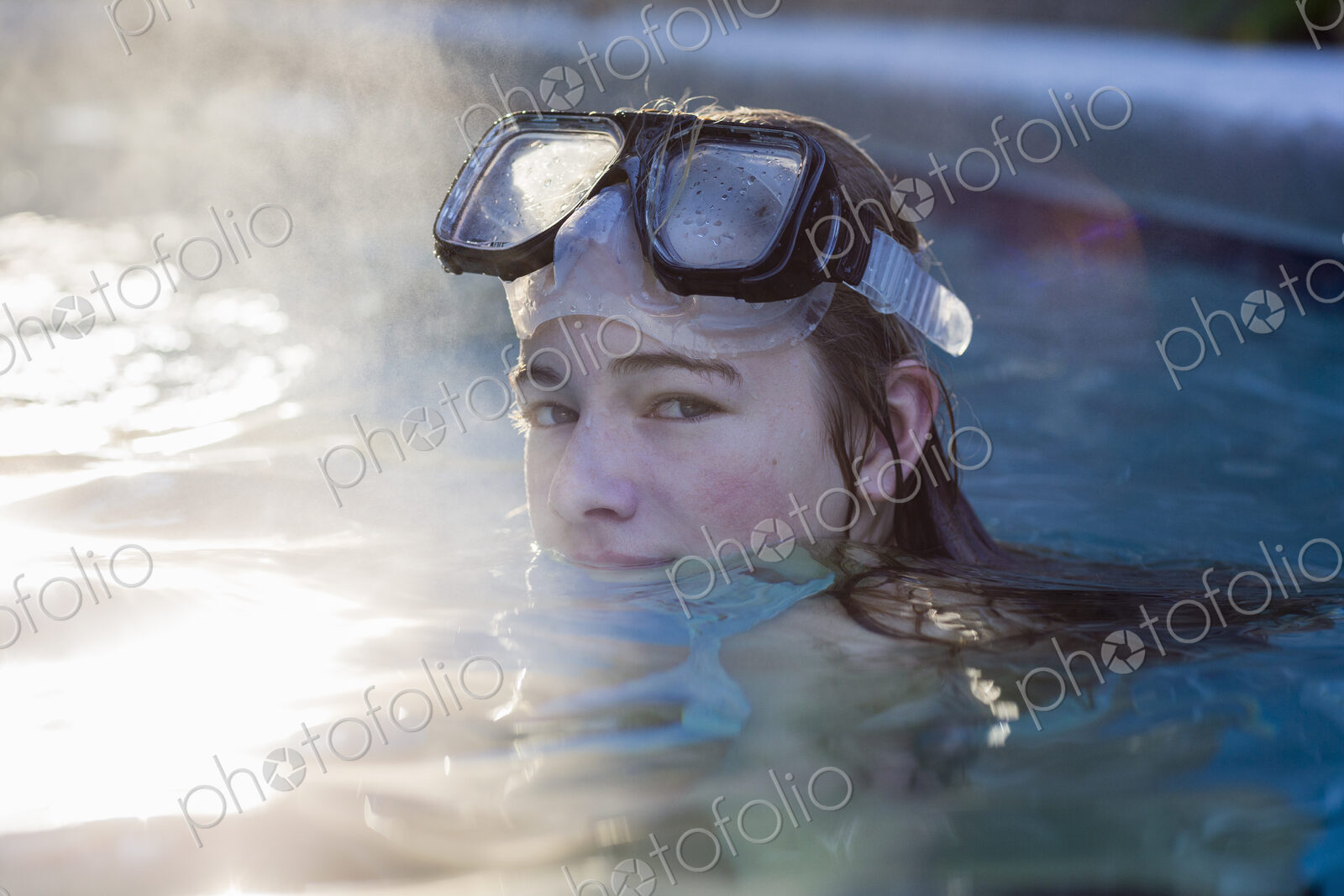 A teenage girl in a swimming pool wearing goggles, steam rising