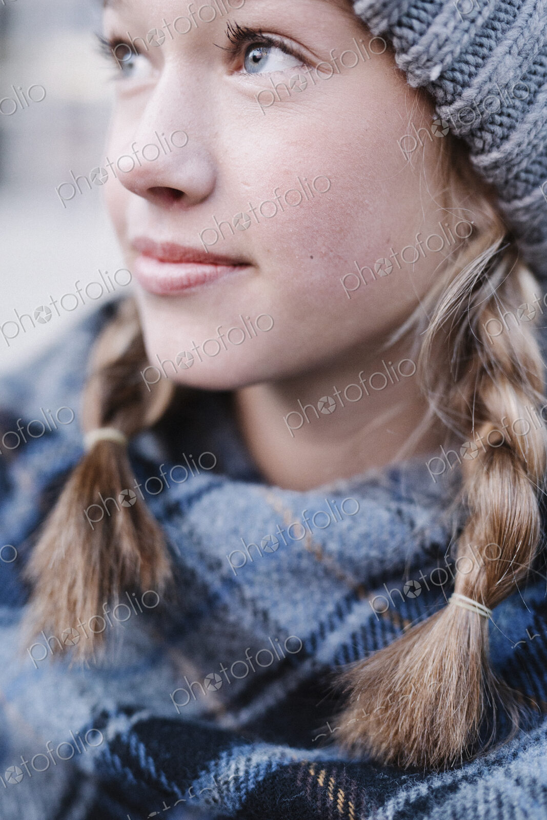 A teenage girl in a tartan plaid shawl and woolly hat outdoors in the winter.