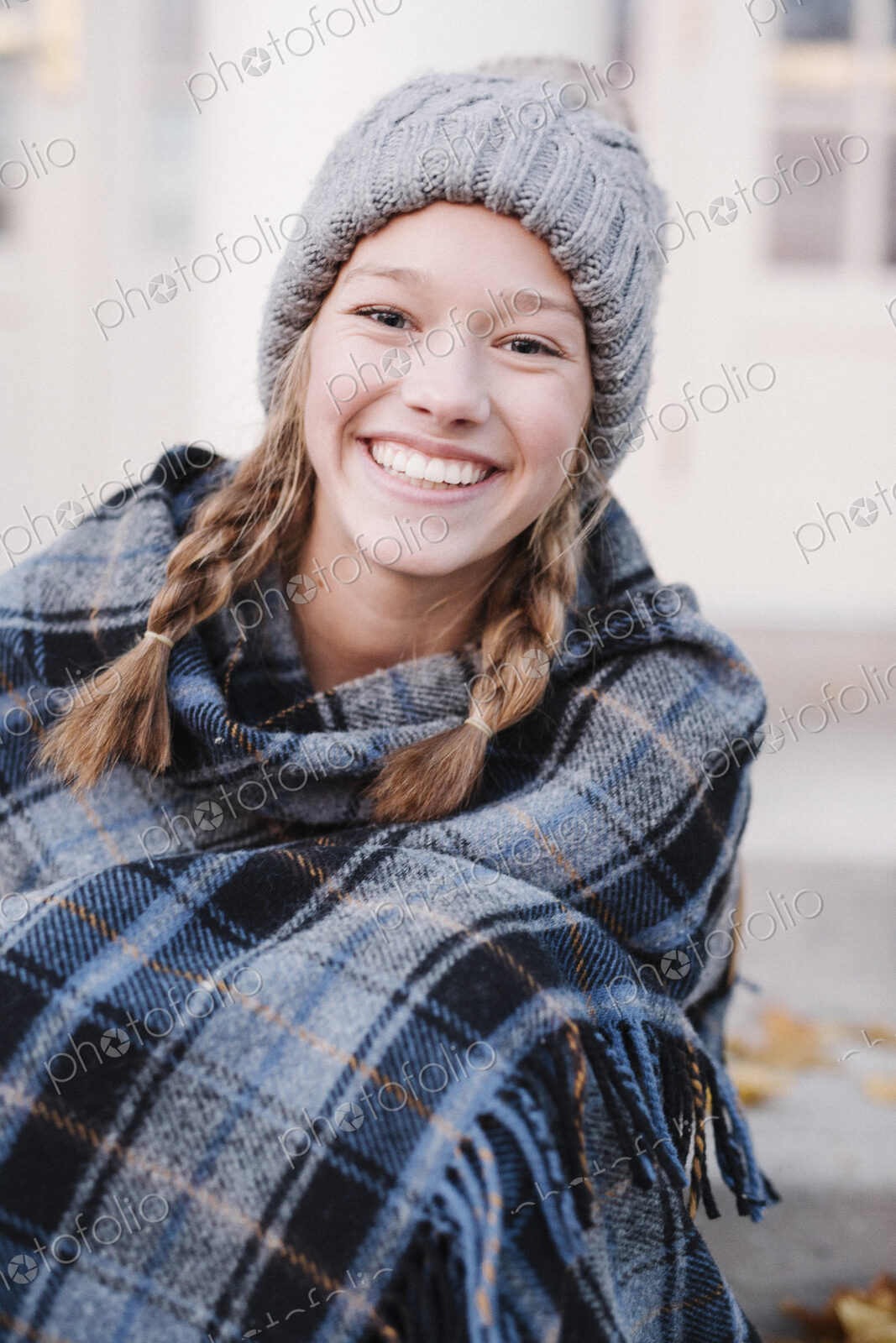 A teenage girl in a tartan plaid shawl and woolly hat outdoors in the winter.