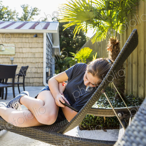 A teenage girl lying on a sun lounger using a smart phone.