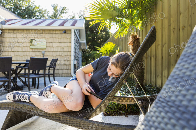 A teenage girl lying on a sun lounger using a smart phone.