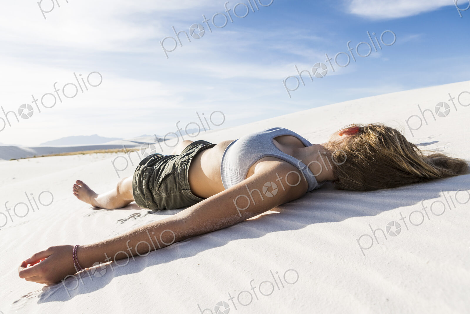 A teenage girl lying on her back on the smooth white sand White Sands Nat’l Monument, NM