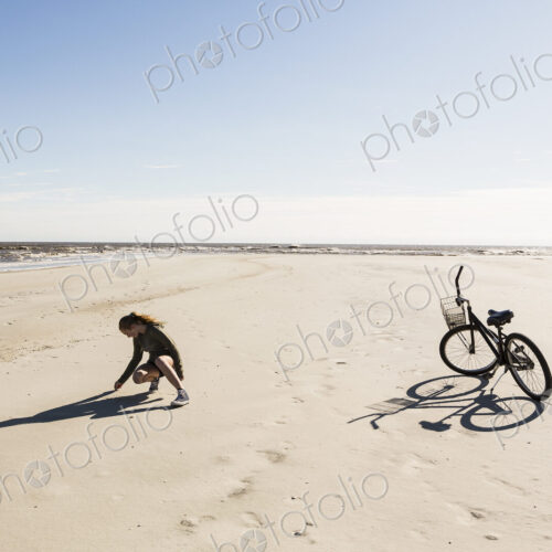 A teenage girl on a wide empty sandy beach collecting shells.
