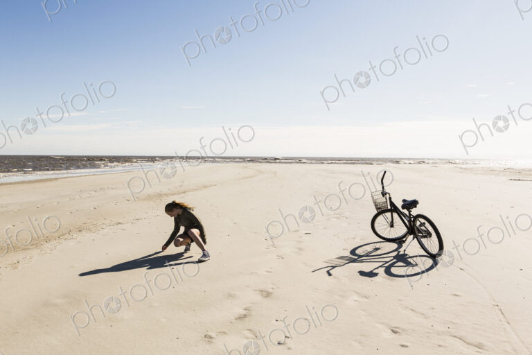 A teenage girl on a wide empty sandy beach collecting shells.