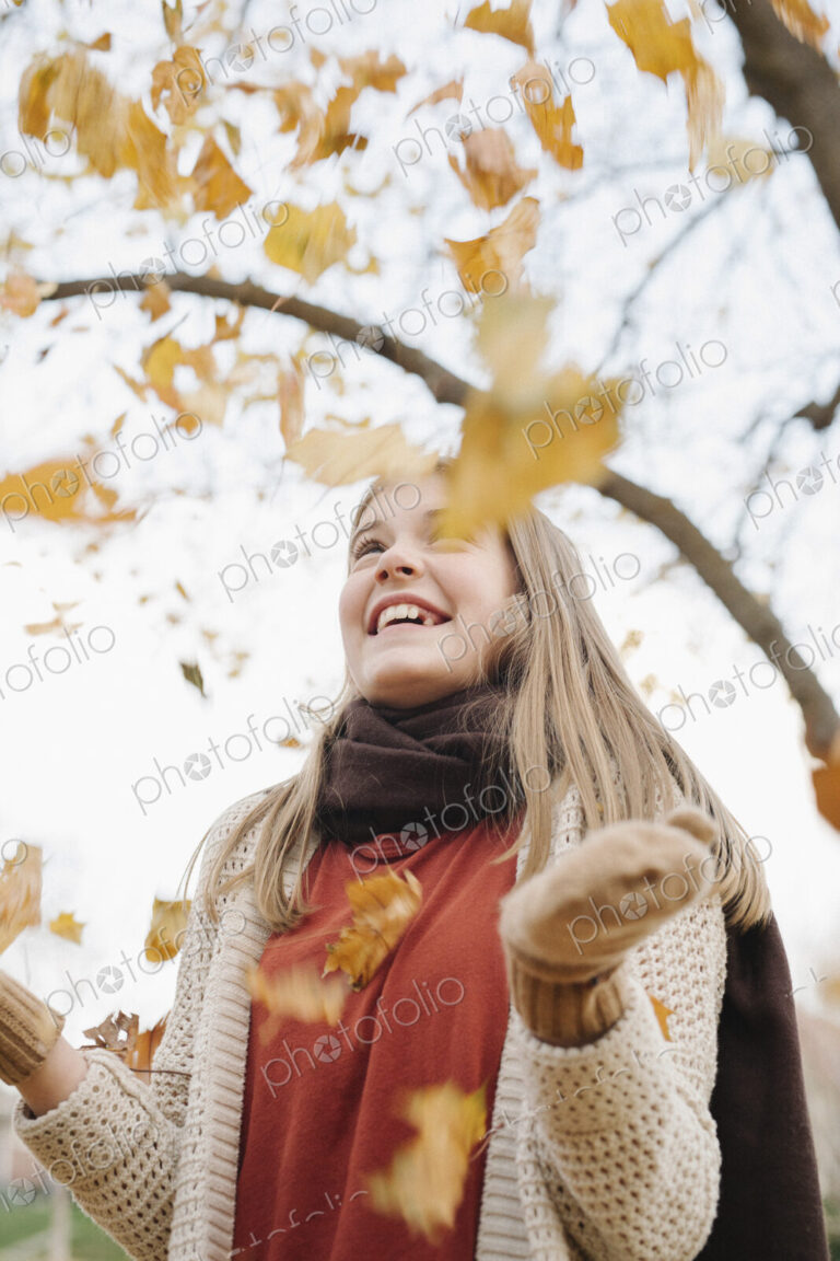 A teenage girl outdoors throwing autumn leaves into the air.