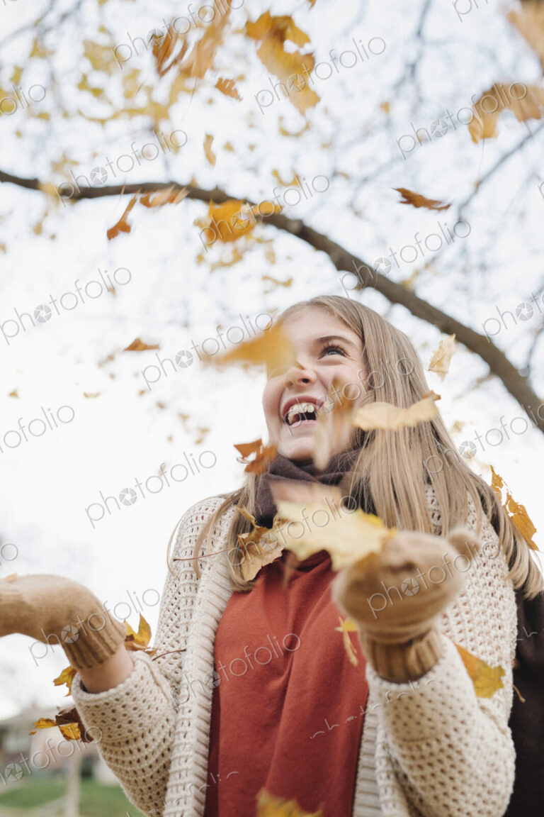 A teenage girl outdoors throwing autumn leaves into the air.
