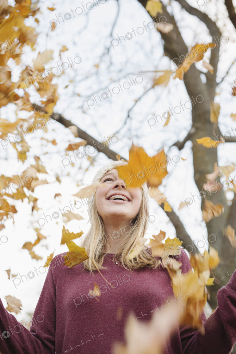 A teenage girl outdoors throwing autumn leaves into the air.