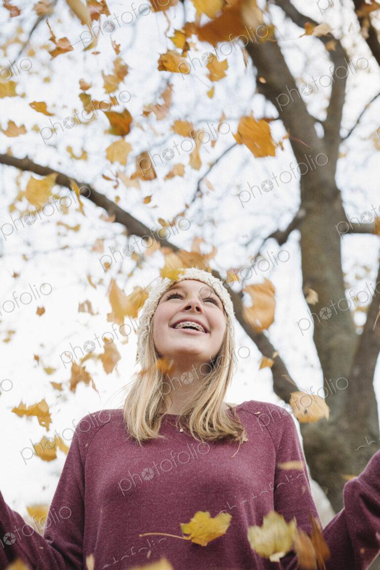 A teenage girl outdoors throwing autumn leaves into the air.