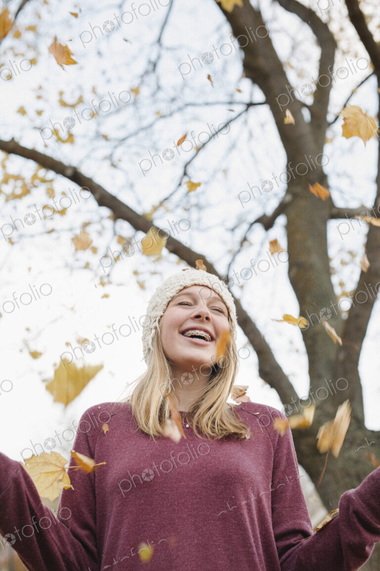 A teenage girl outdoors throwing autumn leaves into the air.