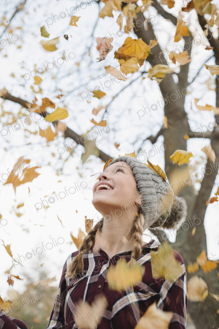A teenage girl outdoors throwing autumn leaves into the air.