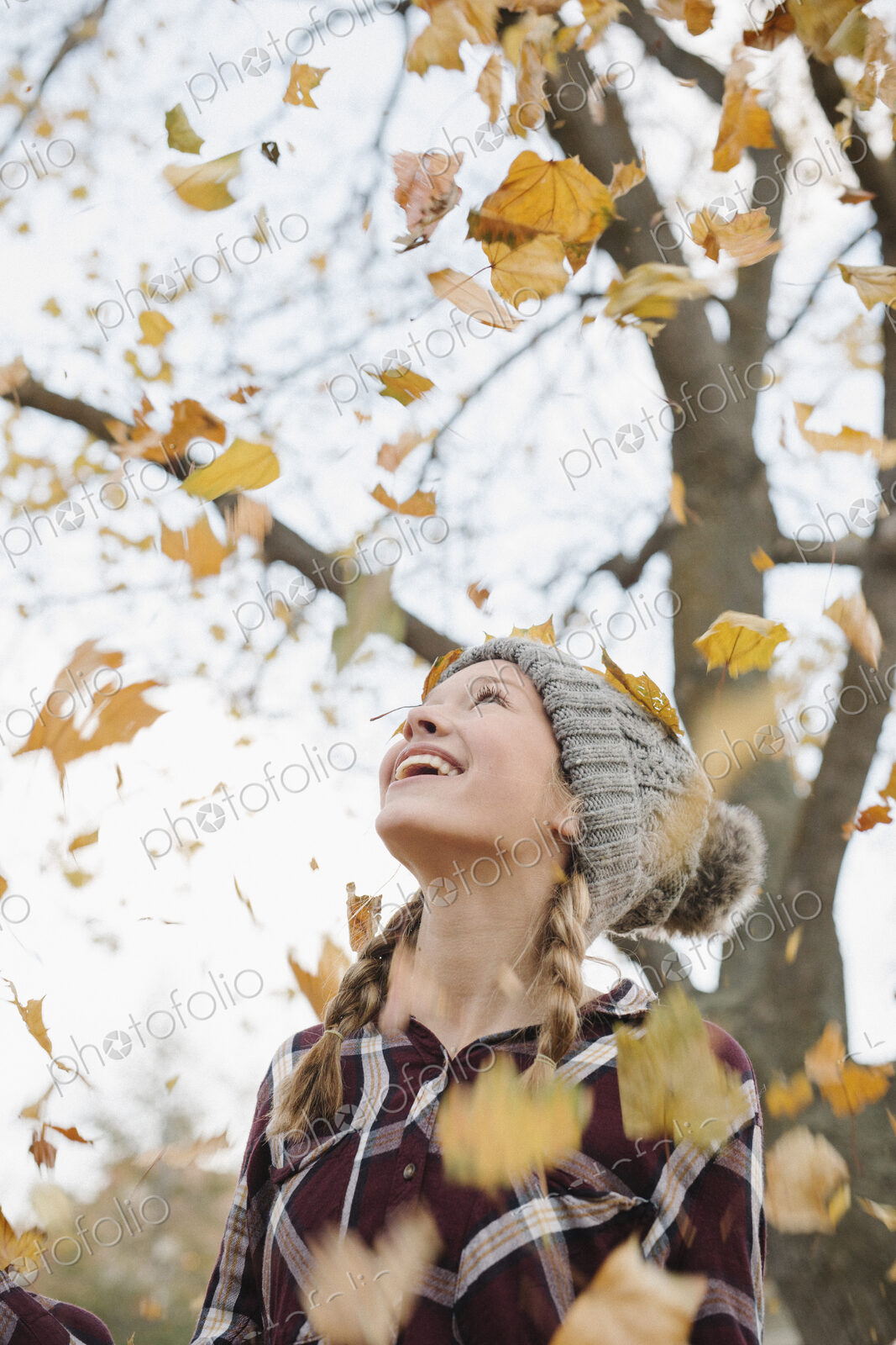 A teenage girl outdoors throwing autumn leaves into the air.