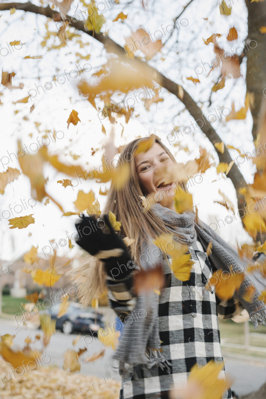 A teenage girl outdoors throwing autumn leaves into the air.