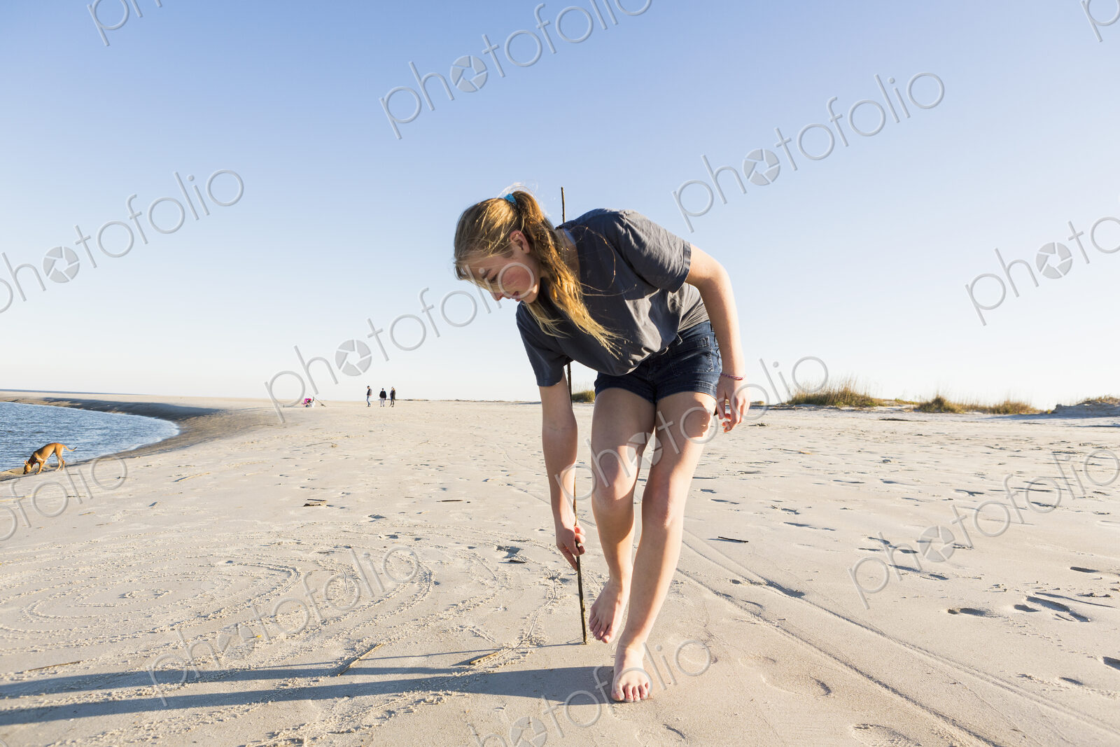 A teenage girl playing in sand dunes, at the beach