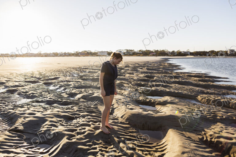 A teenage girl playing in sand dunes, at the beach
