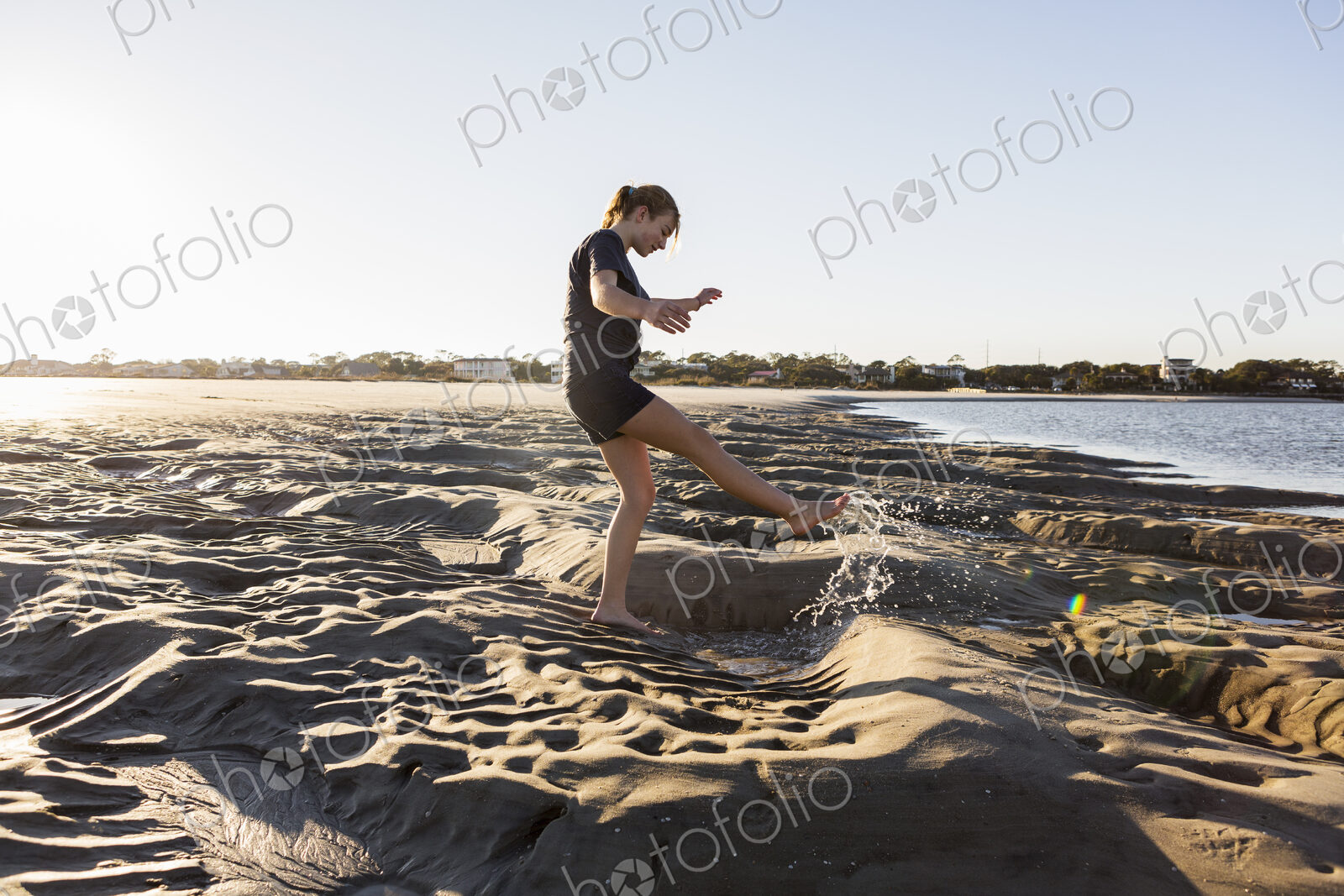 A teenage girl playing in sand dunes, at the beach