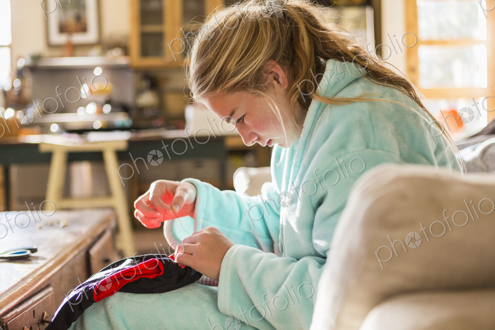A teenage girl sewing a shirt sitting in her bathrobe.