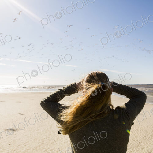 A teenage girl standing on a wide open beach, looking into the distance.