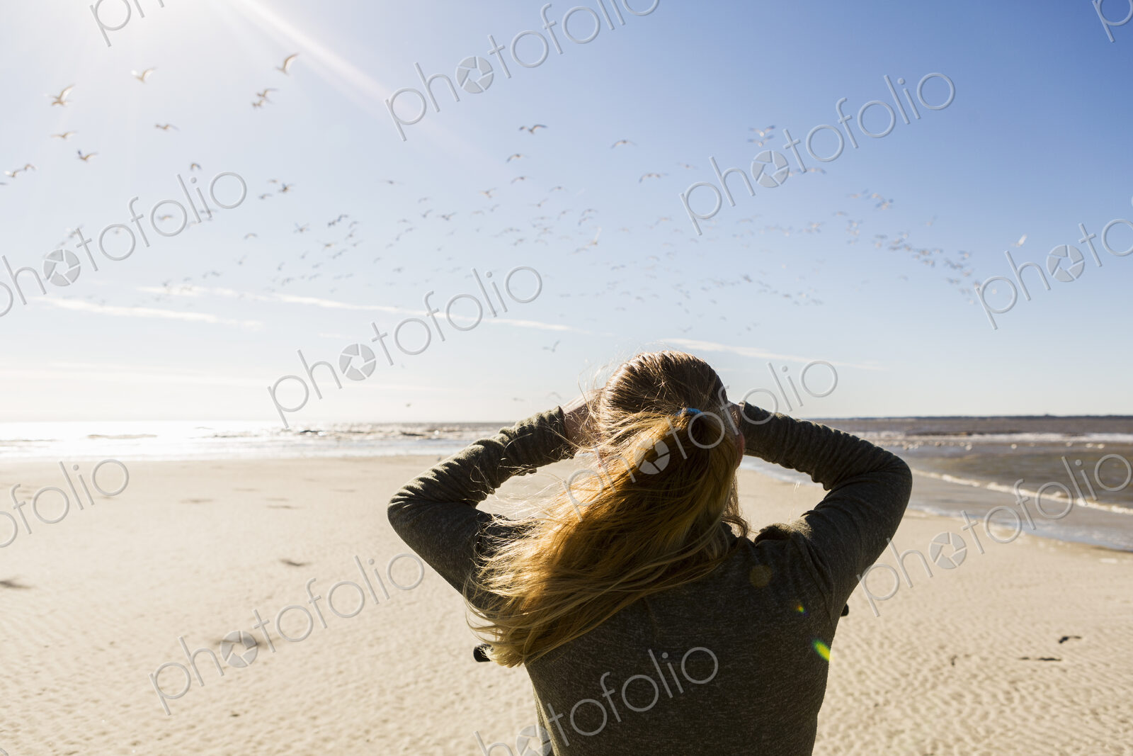 A teenage girl standing on a wide open beach, looking into the distance.