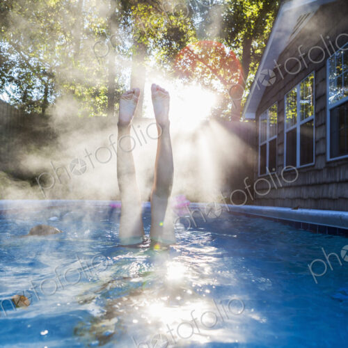 A teenage girl swimming in a pool, diving into warm water, steam rising.