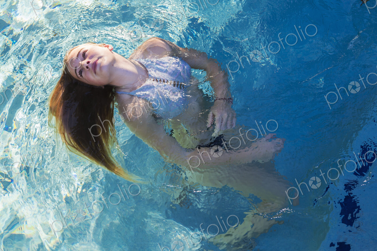 A teenage girl swimming in a pool, floating head back hair spread on the water.