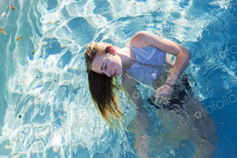 A teenage girl swimming in a pool, head back hair floating in the water.