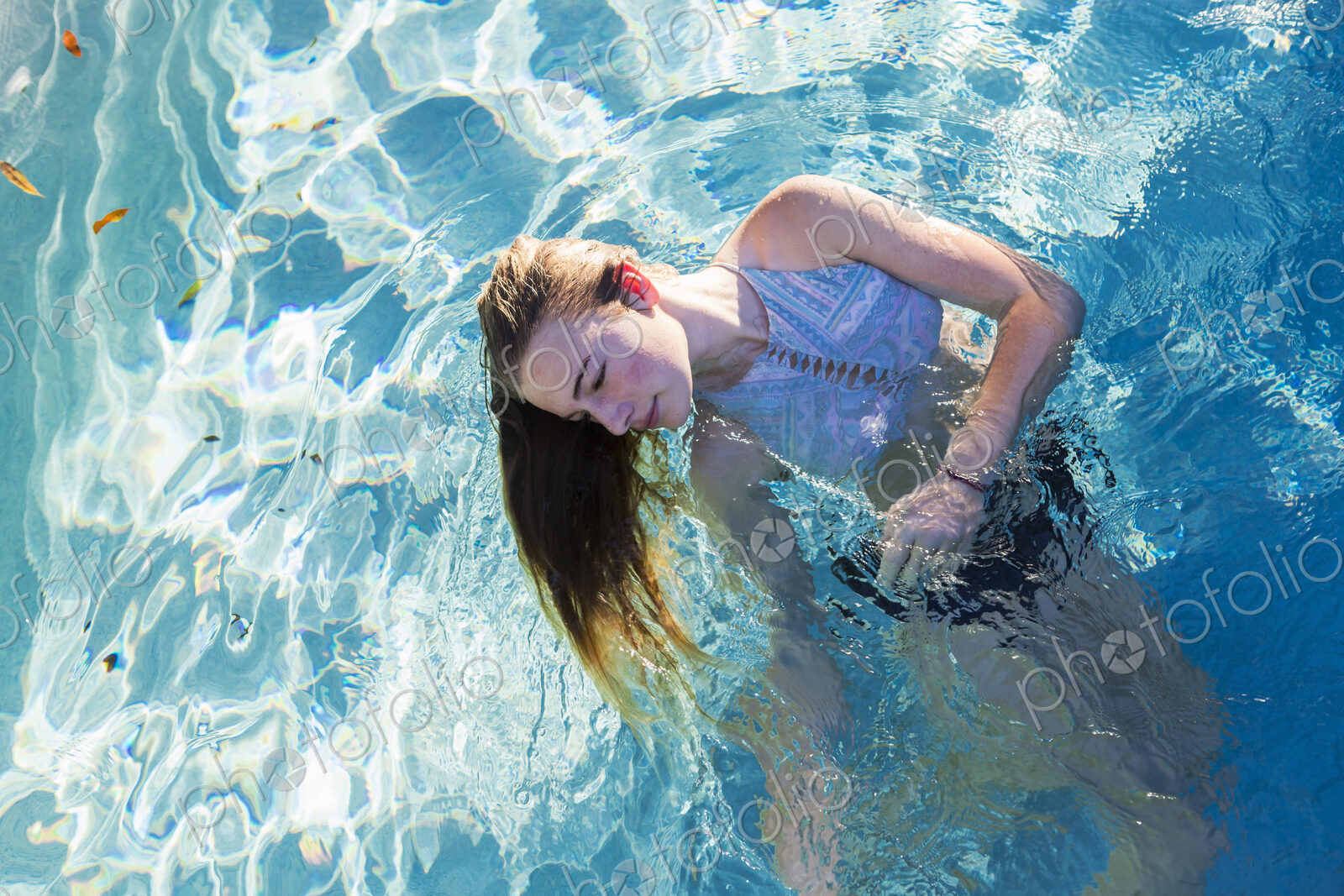 A teenage girl swimming in a pool, head back hair floating in the water.