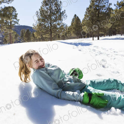 A teenage girl wearing snow shoes lying in the snow laughing