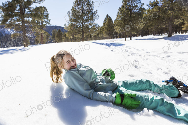 A teenage girl wearing snow shoes lying in the snow laughing