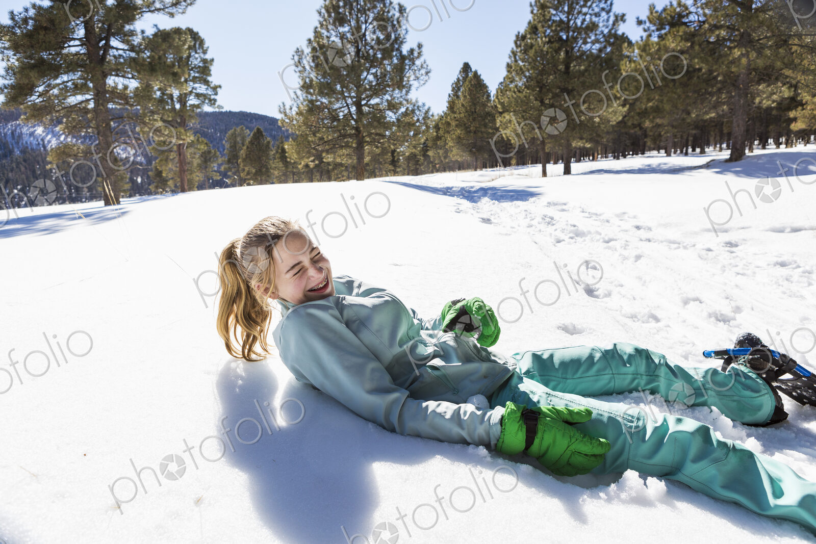 A teenage girl wearing snow shoes lying in the snow laughing